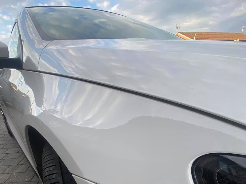 Dent in the front wing of a white car before paintless dent removal